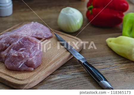 Chicken breast on a cutting board, knife and vegetables on the side 118365173