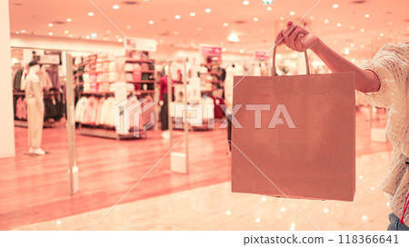 Brown paper bag being held by hand, set against a blurred background of a shopping mall, concept of shopping and Black Friday deals, capturing excitement and rush of retail experiences. 118366641