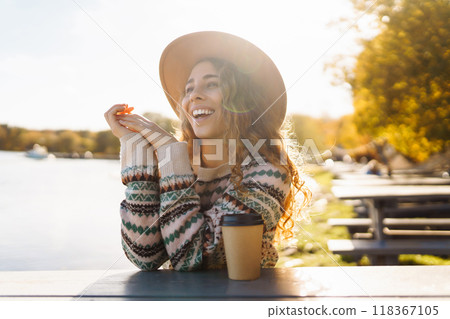 Fall concept woman drinking coffee on bench against backdrop of lake. Enjoying, solitude with nature 118367105