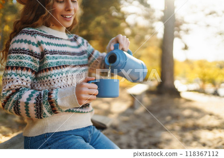 Woman holds thermos and drinks tea in sunny autumn forest. Vacation, travel, lifestyle concept. Woman holds thermos and drinks tea in sunny autumn forest. Vacation, travel, lifestyle concept. 118367112