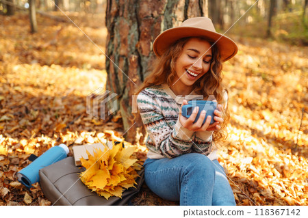 Cute young woman drinks hot drink from thermos and enjoys nature. Autumn landscape. relax concept. 118367142