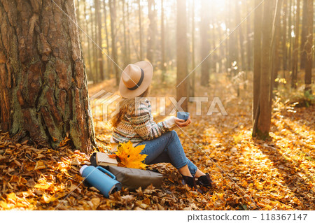 Cute young woman drinks hot drink from thermos and enjoys nature. Autumn landscape. relax concept. Cute young woman drinks hot drink from thermos and enjoys nature. Autumn landscape. relax concept. 118367147