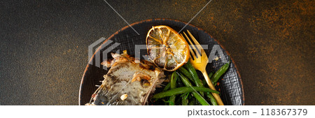 Enjoy a nutritious meal of baked green beans with onions and baked mackerel, beautifully arranged on a plate against a brown background banner 118367379