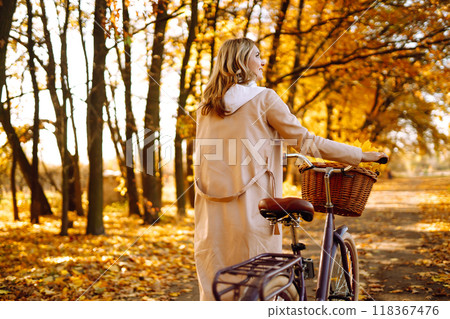 Stylish woman with a bicycle enjoying autumn weather in the park. Beautiful Woman in the autumn forest. Stylish woman with a bicycle enjoying autumn weather in the park. Beautiful Woman in the autumn forest. 118367476