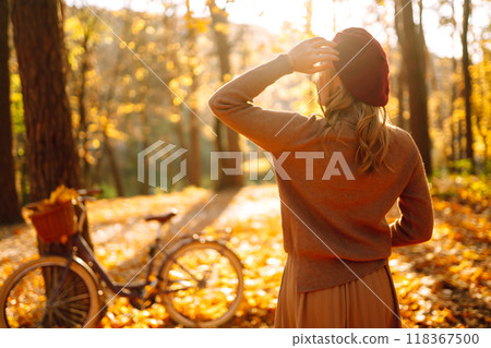 Stylish woman with a bicycle enjoying autumn weather in the park. Beautiful Woman in the autumn forest. Stylish woman with a bicycle enjoying autumn weather in the park. Beautiful Woman in the autumn forest. 118367500