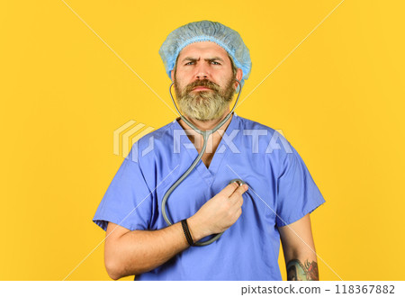 Doctor in blue medical coat. Polyclinic and hospital. bearded doctor use phonendoscope. listening his heart beating. Pathogen leads to pneumonia. heart attack. virus infection from china Doctor in blue medical coat. Polyclinic and hospital. bearded doctor use phonendoscope. listening his heart beating. Pathogen leads to pneumonia. heart attack. virus infection from china 118367882