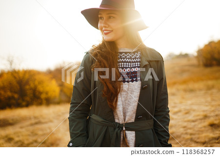 Beautiful stylish girl walks in the autumn park. The girl is dressed in a green coat and a red hat. 118368257