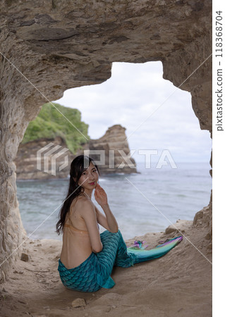 一條年輕的女美人魚坐在一個俯瞰大海的洞穴裡，回頭望去 118368704