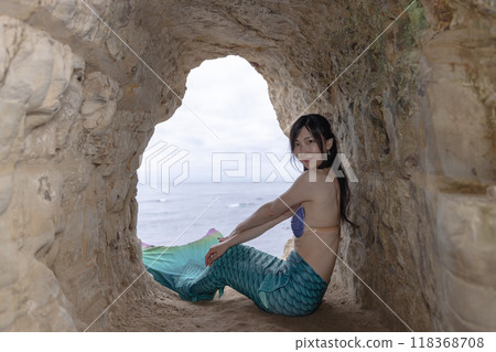 一條年輕的女美人魚坐在一個俯瞰大海的洞穴裡，回頭望去 118368708