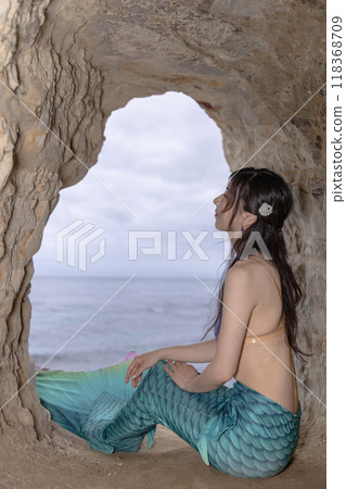 年輕的女美人魚坐在俯瞰大海的洞穴裡 118368709