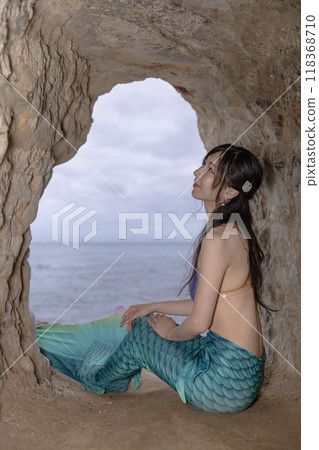 Young female mermaid sitting in a cave overlooking the sea 118368710