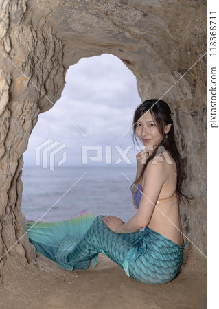 一條年輕的女美人魚坐在一個俯瞰大海的洞穴裡,回頭望去 一條年輕的女美人魚坐在一個俯瞰大海的洞穴裡,回頭望去 118368711