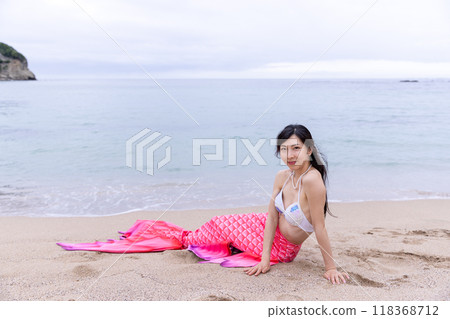 一個年輕的女美人魚坐在沙灘上看著你 118368712