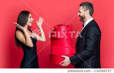 Valentines day. Couple gives present to the Valentines Day. Man and woman hold gift. Elegant couple on red. Exchange of gifts. Romantic day together. Love present for anniversary. Mutual surprise Valentines day. Couple gives present to the Valentines Day. Man and woman hold gift. Elegant couple on red. Exchange of gifts. Romantic day together. Love present for anniversary. Mutual surprise 118368737