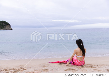 年輕的女美人魚坐在海邊的沙灘上 118368963