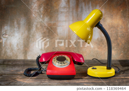 A table lamp and a red vintage phone on old boards against a shabby background A table lamp and a red vintage phone on old boards against a shabby background 118369464