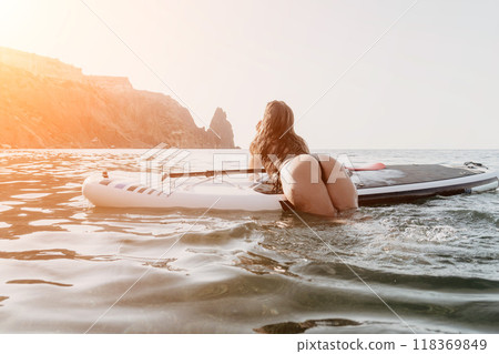 Woman Paddleboard Ocean - A woman in a bikini lies on a paddleboard in the ocean, looking out at the mountains in the distance. 118369849