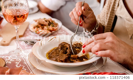 Close-up of a plate of meat in sauce while a woman eats at Christmas Close-up of a plate of meat in sauce while a woman eats at Christmas 118371406