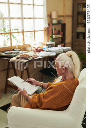 Senior Woman Sitting Indoors Reading Book Peacefully Senior Woman Sitting Indoors Reading Book Peacefully 118373405