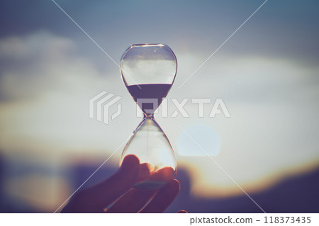 A person's hand holding a glass hourglass 118373435