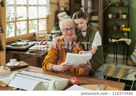 Elderly Woman Reading Papers with Young Girl in Cozy Room Elderly Woman Reading Papers with Young Girl in Cozy Room 118373480