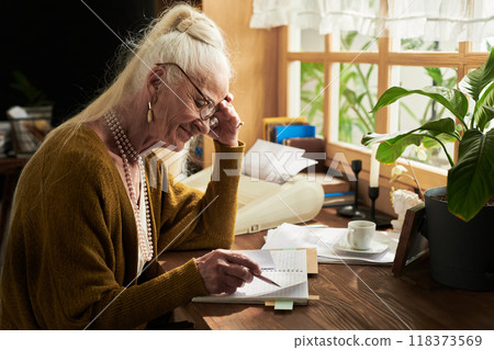 Senior Woman Writing in Notebook at Cozy Desk Senior Woman Writing in Notebook at Cozy Desk 118373569