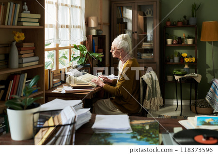 Senior Woman Reading Documents by Window in Cozy Room Senior Woman Reading Documents by Window in Cozy Room 118373596