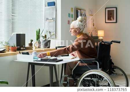 Senior Woman Sitting in Wheelchair Working By Window Senior Woman Sitting in Wheelchair Working By Window 118373765