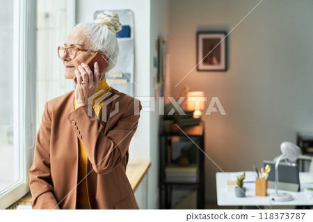 Elderly Woman Talking on Smartphone by Window Elderly Woman Talking on Smartphone by Window 118373787