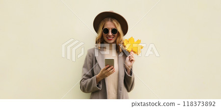 Autumn portrait stylish happy smiling young woman with phone, beautiful girl holding yellow leaves 118373892