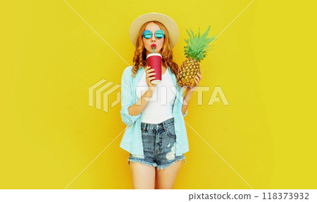 Portrait young woman drinking juice, holding pineapple in summer hat on colorful yellow background 118373932