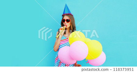 Portrait of cheerful young woman in a birthday cap with colorful balloons on a blue background Portrait of cheerful young woman in a birthday cap with colorful balloons on a blue background 118373951