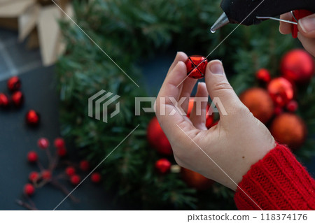 Crafter using hot glue Step by step instruction of making handmade Christmas wreath made of festive decorations in red color. Female hands creating craft homemade decor. New year celebration. Winter 118374176