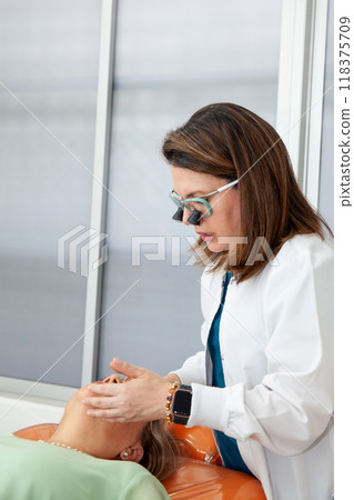 Dermatologist  making a routine checkup on a senior famale patient using a binocular loupe. 118375709