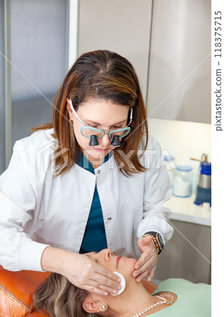 Dermatologist  making a routine checkup on a senior famale patient using a binocular loupe. 118375715