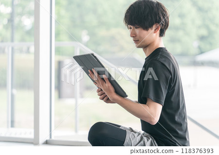 Young Asian man in sportswear using a tablet computer Young Asian man in sportswear using a tablet computer 118376393