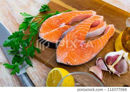Raw salmon steaks on wooden cutting board with greens, lemon and garlic Raw salmon steaks on wooden cutting board with greens, lemon and garlic 118377066