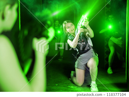 Joyous girl with laser pistol playing laser tag with girlfriends on labyrinth Joyous girl with laser pistol playing laser tag with girlfriends on labyrinth 118377104