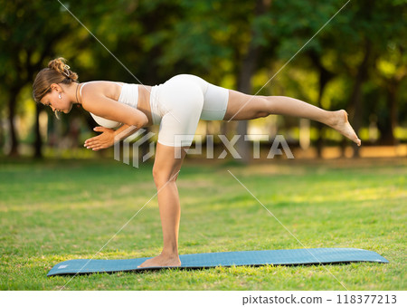 Girl in park on green grass of lawn performs Natarajasana Girl in park on green grass of lawn performs Natarajasana 118377213