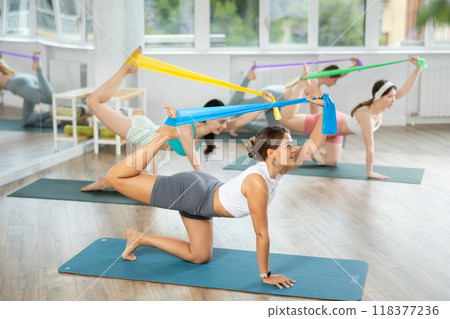Girl leads class women, standing on all fours, performing exercises with wide elastic skip rope 118377236