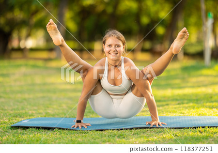 Girl performing Firefly pose, arm-balancing yoga asana in summer park 118377251