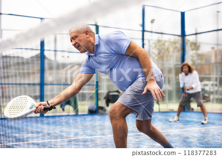 View through the tennis net at an elderly player in game of padel View through the tennis net at an elderly player in game of padel 118377283