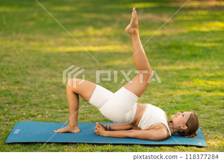 Girl in park on green grass of lawn performs Setu Bandha Sarvangasana 118377284