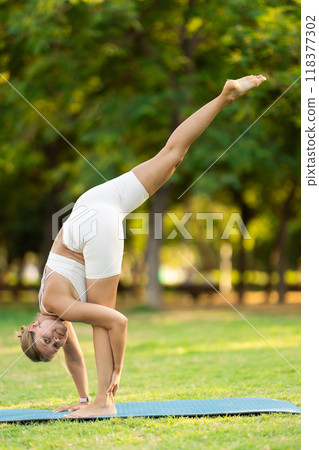 Girl in park on green grass of lawn performs eka padasana 118377302