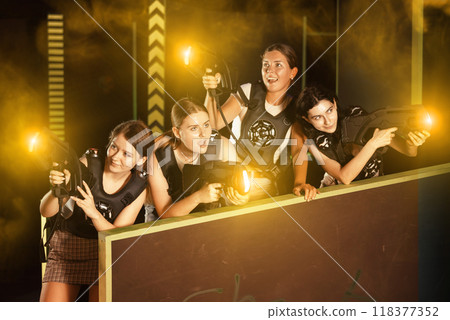 Four positive girlfriends playing enthusiastically laser tag in dark room 118377352