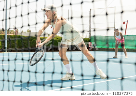 Active aged woman plays tennis on court. View through tennis net 118377375