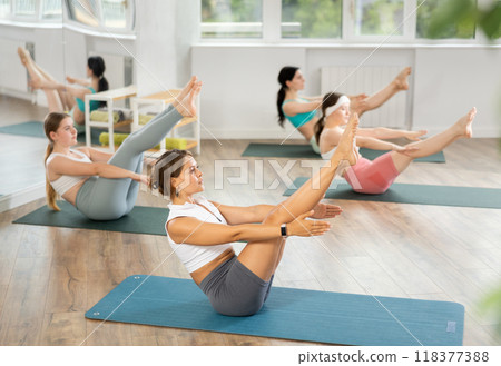 Young female participant working out Paripurna Navasana, boat pose with students group 118377388