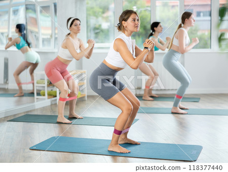 Young woman during Pilates strength training performs squats with elastic band on legs and shins Young woman during Pilates strength training performs squats with elastic band on legs and shins 118377440