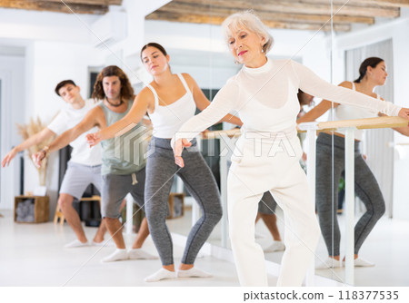 Elderly female dancer exercise near the ballet barre at a group training session in the dance studio. Elderly female dancer exercise near the ballet barre at a group training session in the dance studio. 118377535