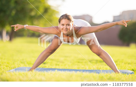 Girl in park on green grass of lawn performs Himavanasana 118377558